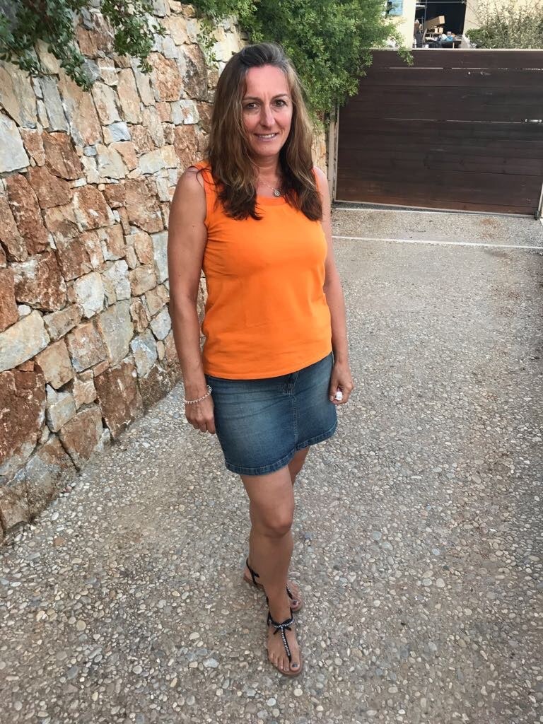 A photograph of Anna, a woman smiling and standing by a rock wall during summer.