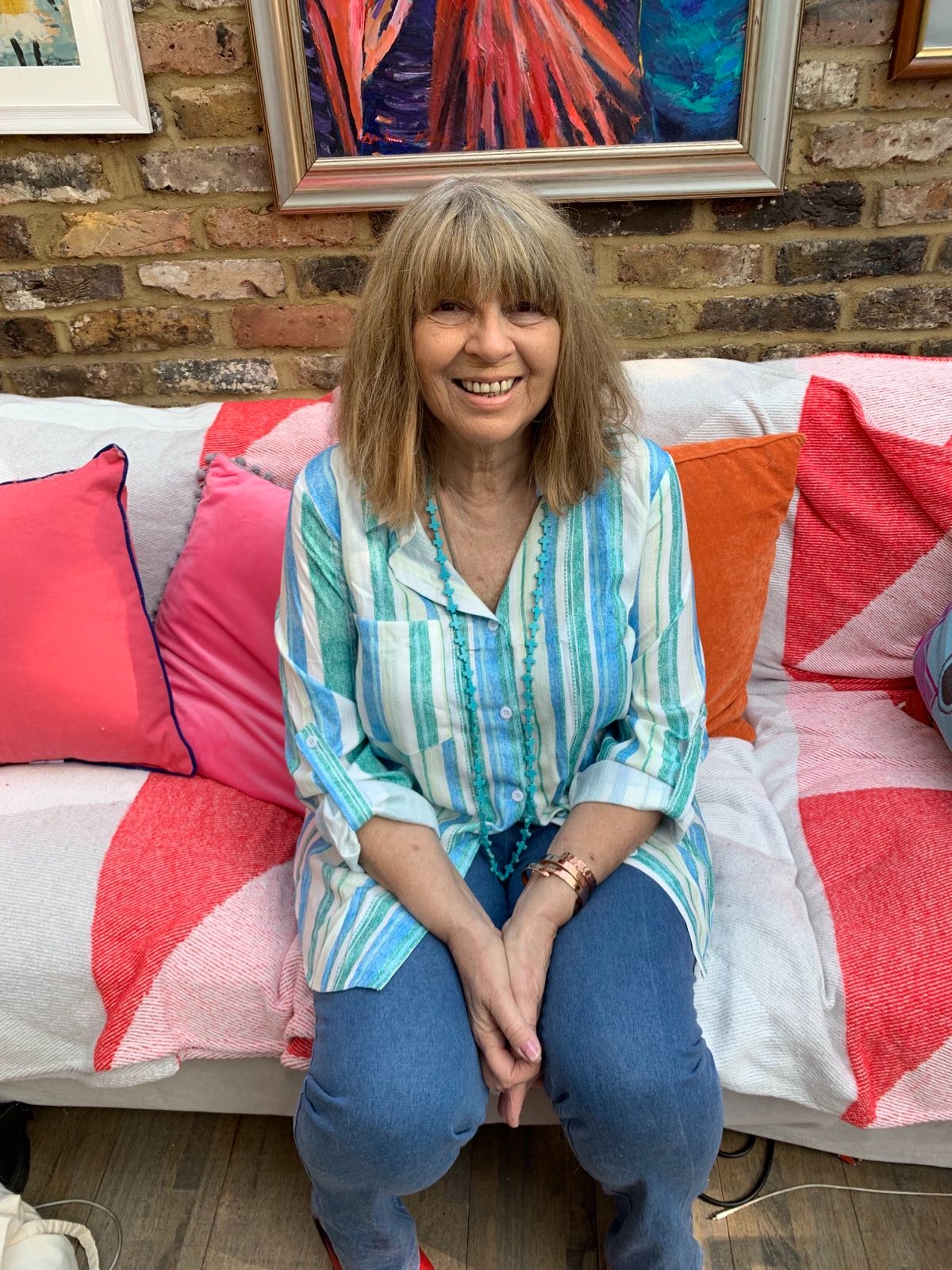 A photograph of Barbara, a woman smiling and sitting on a sofa.